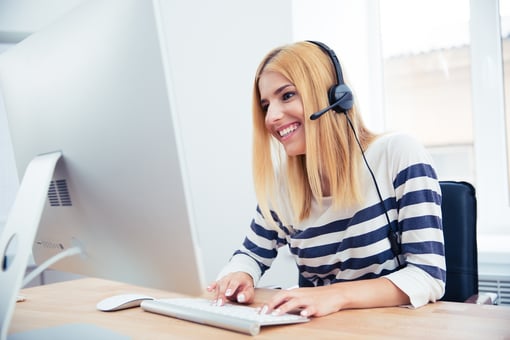 Cheerful young female operator with headset using desktop computer in office