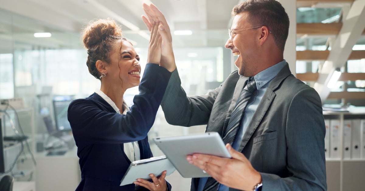 A male and female executive share a high-five as their business meets and exceeds strategic goals. 