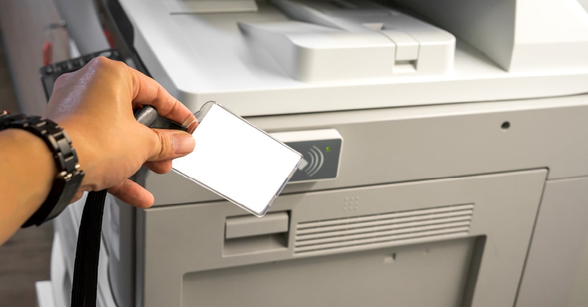 A student swipes a badge in front of a university printer to track use and recover costs.