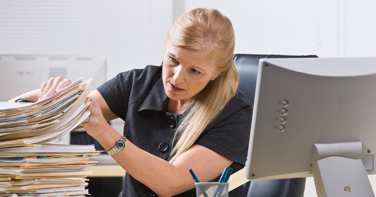 A female lawyer struggles with the amount of paper documents on her desk.