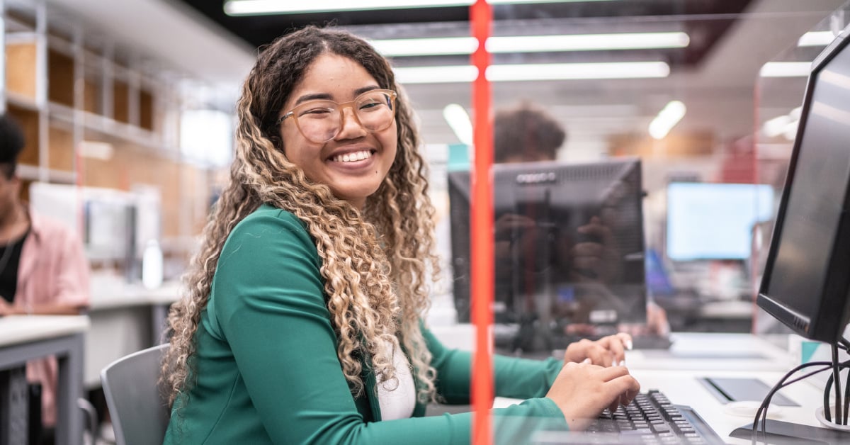 A happy university student working on her computer in the campus library.