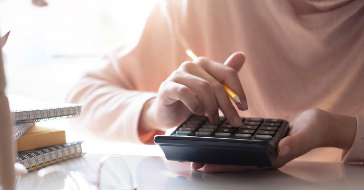 A female business owner calculates the cost of per-user priced managed IT services vs its ROI on a calculator.